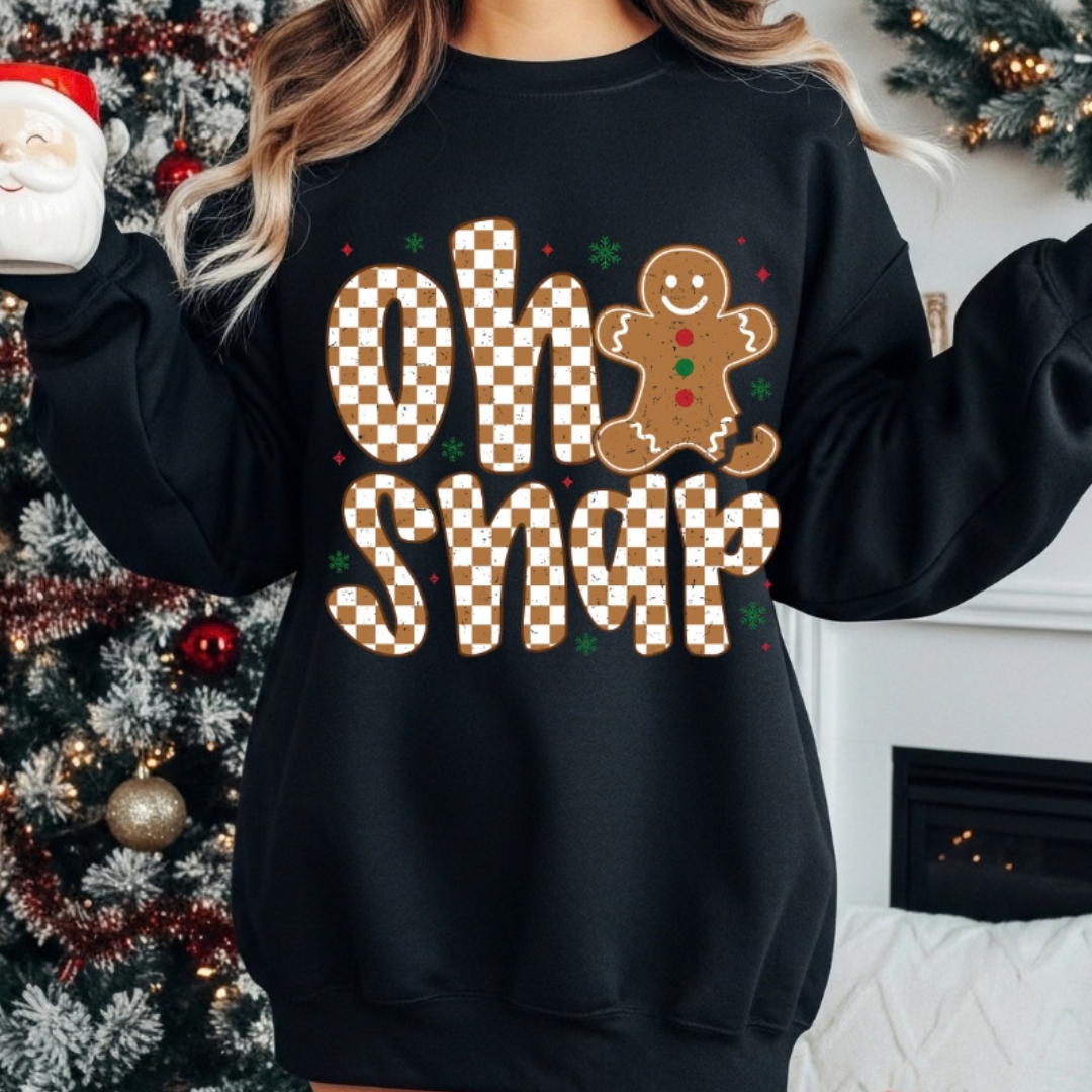 Model in a black sweatshirt printed with Oh Snap in checkered lettering beside a gingerbread man.