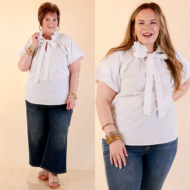 Models are wearing Short Puff Sleeve Tie Neck Blouse with Gathered Neckline in White with Jeans against a beige backdrop. 