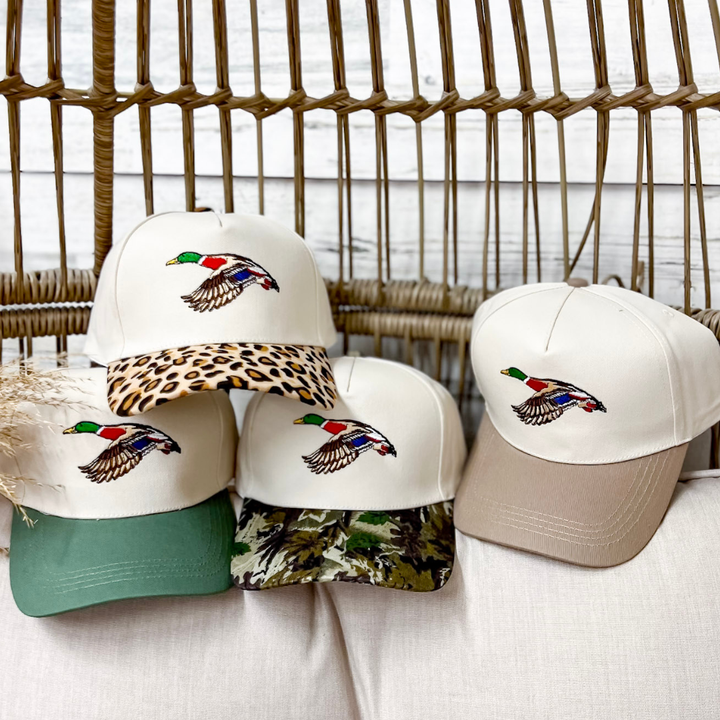 Mallard Two-Tone Canvas Trucker Cap featuring an embroidered flying mallard duck on a cream canvas crown with Forest Green, Camo, Leopard, or Mocha brim and an adjustable snapback closure.