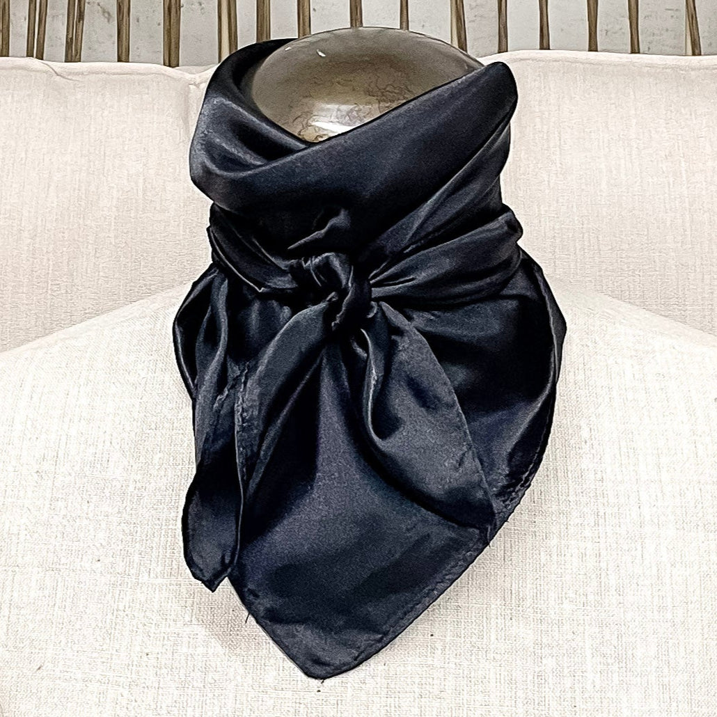 A mannequin sitting on a rustic chair with a black solid mini wild rag tied around its neck.