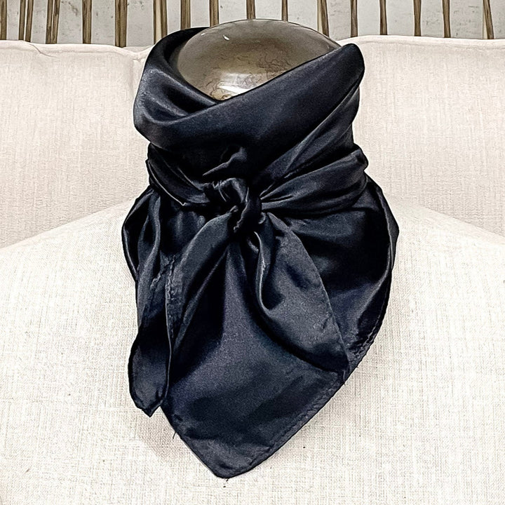 A mannequin sitting on a rustic chair with a black solid mini wild rag tied around its neck.