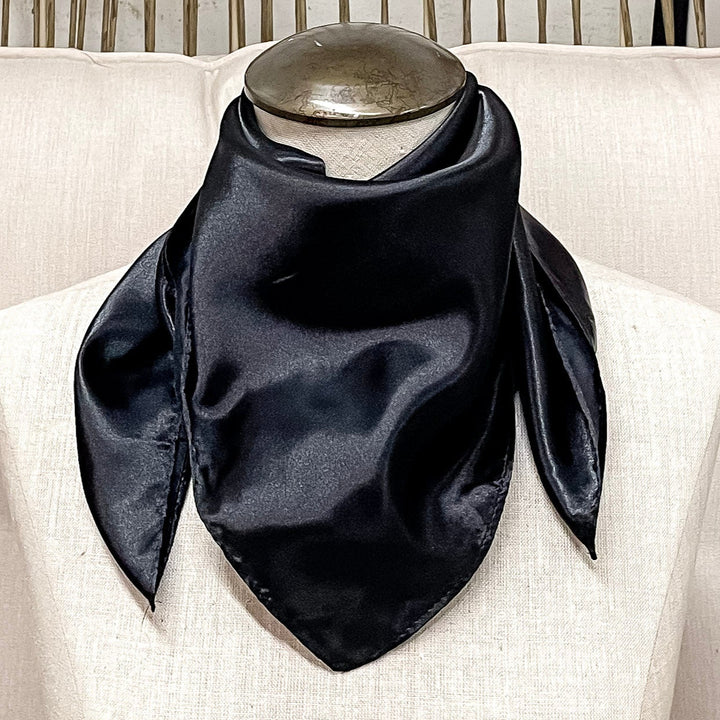 A mannequin sitting on a rustic chair with a black solid mini wild rag around its neck.