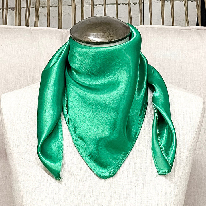 A mannequin sitting on a rustic chair with a green solid mini wild rag around its neck.