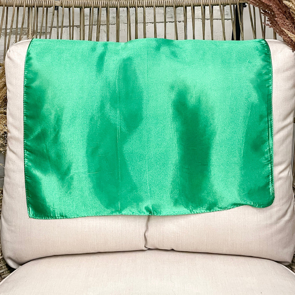 A solid green wild rag laid open on a chair with a wooden rustic background.