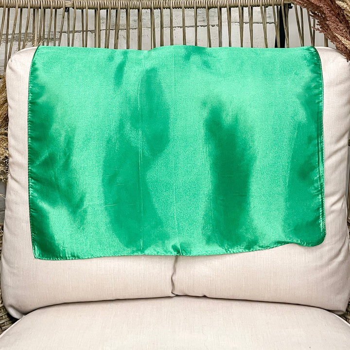 A solid green wild rag laid open on a chair with a wooden rustic background.