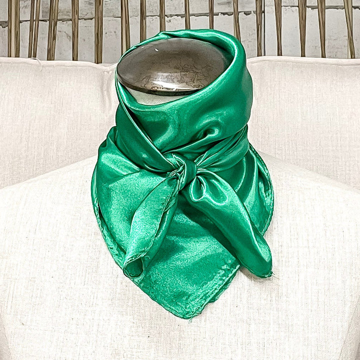 A mannequin sitting on a rustic chair with a green solid mini wild rag tied around its neck.
