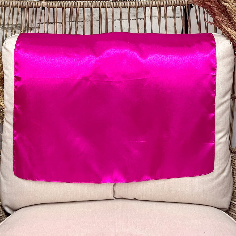 A solid hot pink wild rag laid open on a chair with a wooden rustic background.