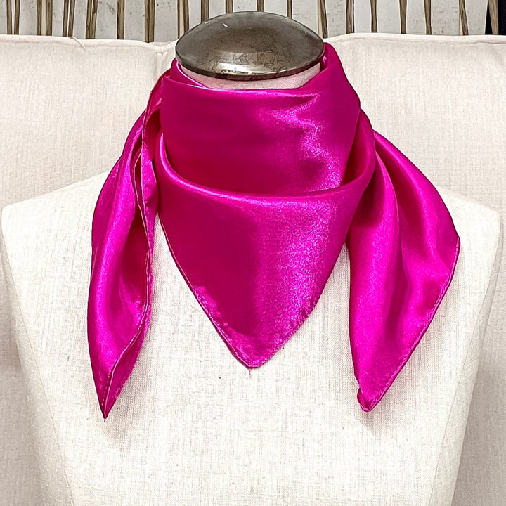 A mannequin sitting on a rustic chair with a hot pink solid mini wild rag around its neck.