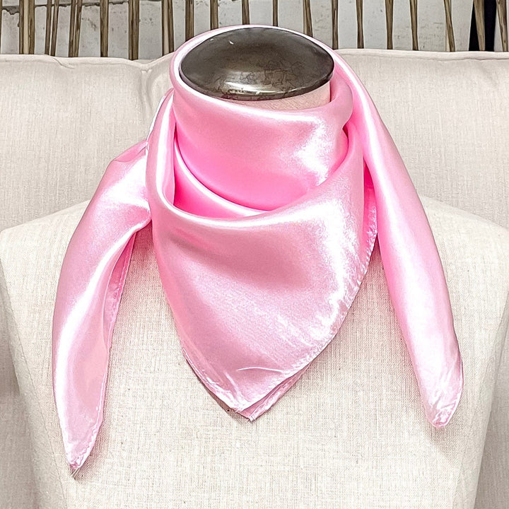 A mannequin sitting on a rustic chair with a light pink solid mini wild rag around its neck.