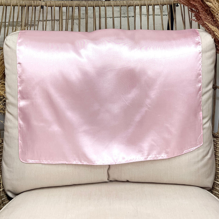 A solid light pink wild rag laid open on a chair with a wooden rustic background.