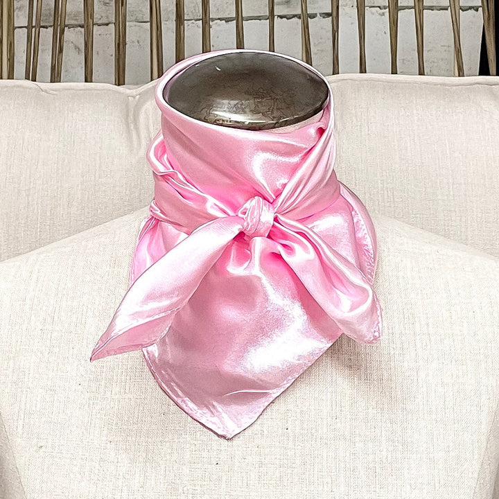 A mannequin sitting on a rustic chair with a light pink solid mini wild rag tied around its neck.