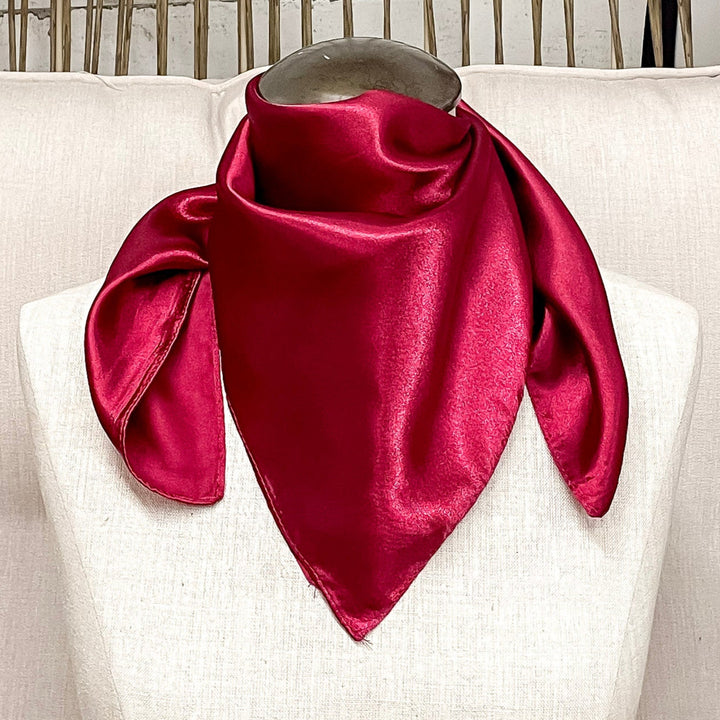A mannequin sitting on a rustic chair with a red solid mini wild rag around its neck.