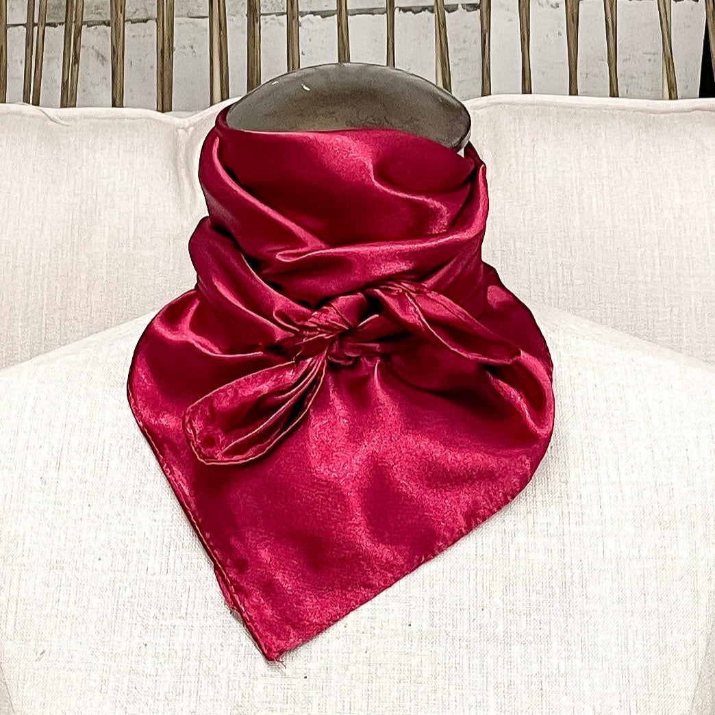 A mannequin sitting on a rustic chair with a red solid mini wild rag tied around its neck.