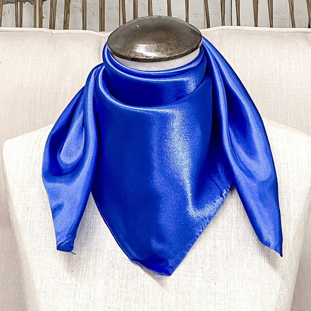 A mannequin sitting on a rustic chair with a royal blue solid mini wild rag around its neck. 