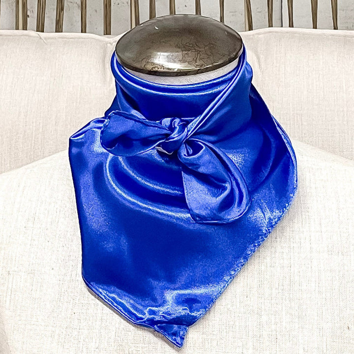 A mannequin sitting on a rustic chair with a royal blue solid mini wild rag tied around its neck.