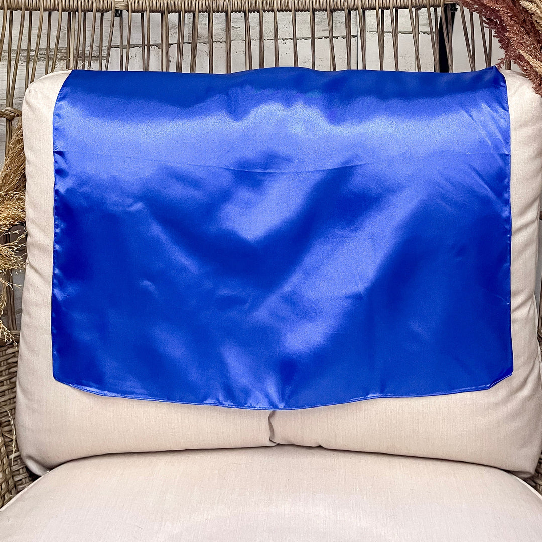 A solid royal blue wild rag laid open on a chair with a wooden rustic background.