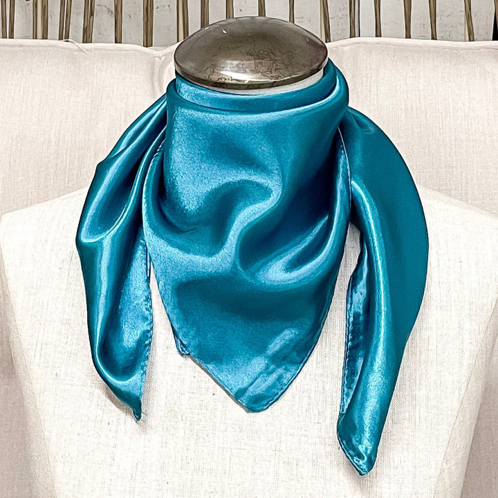 A mannequin sitting on a rustic chair with a turquoise solid mini wild rag around its neck.