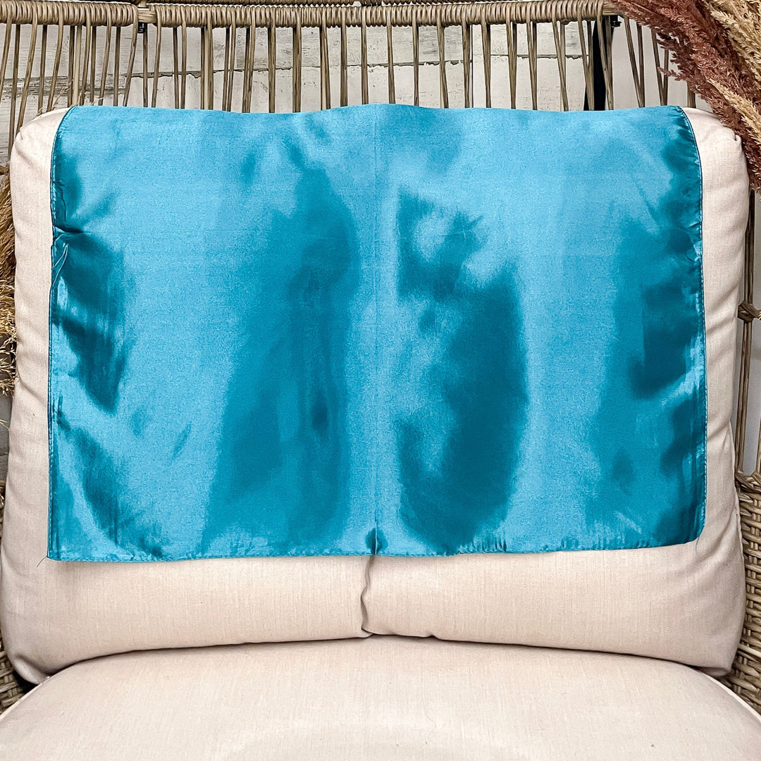A solid turquoise wild rag laid open on a chair with a wooden rustic background.