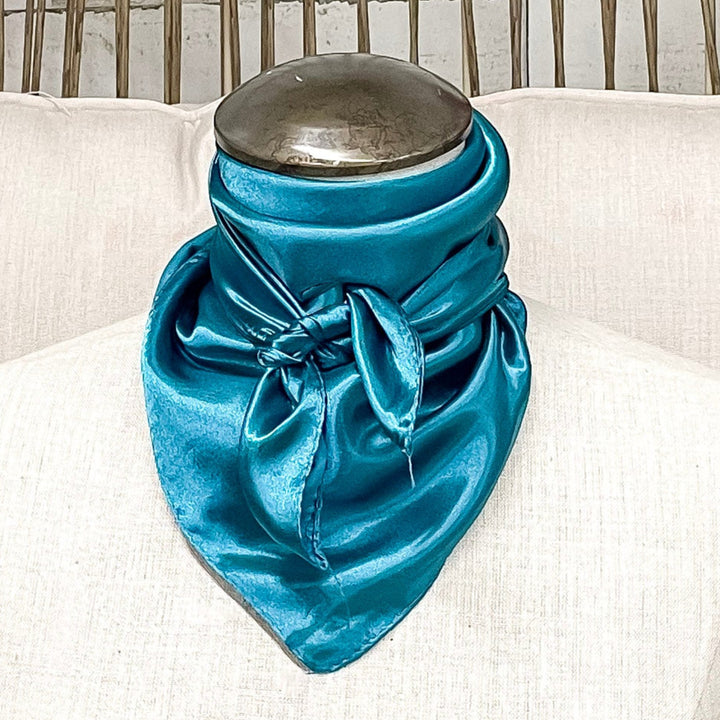 A mannequin sitting on a rustic chair with a turquoise solid mini wild rag tied around its neck.