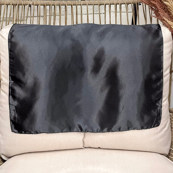 A solid black wild rag laid open on a chair with a wooden rustic background.