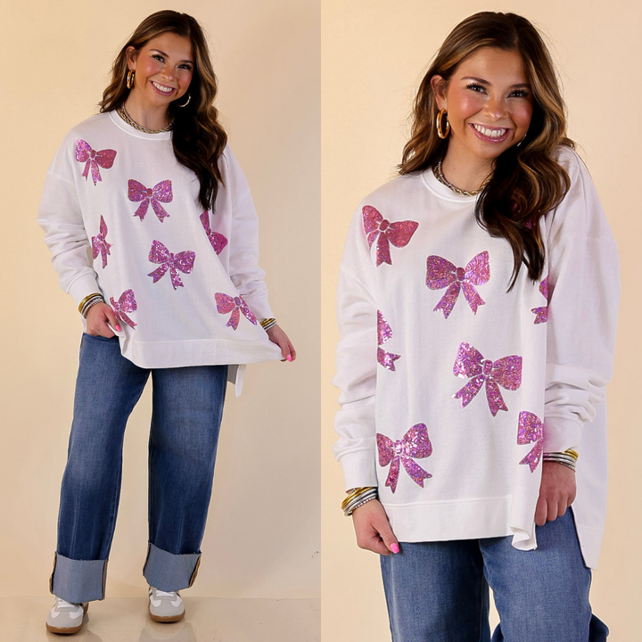 Model is wearing MudPie white sweater with sequined pink bows with jeans on a beige background