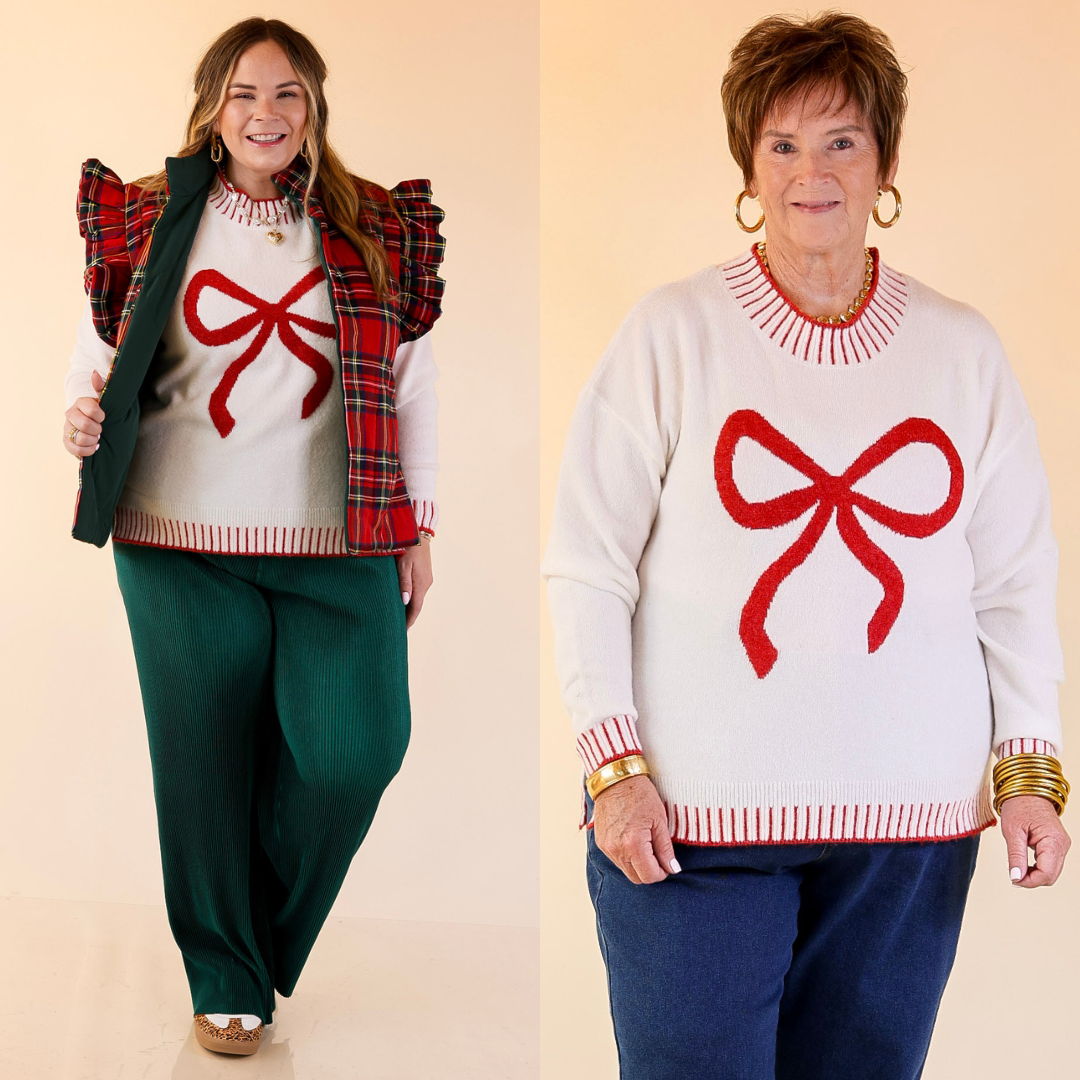 Two women wearing white sweaters with red bow designs against a beige background.