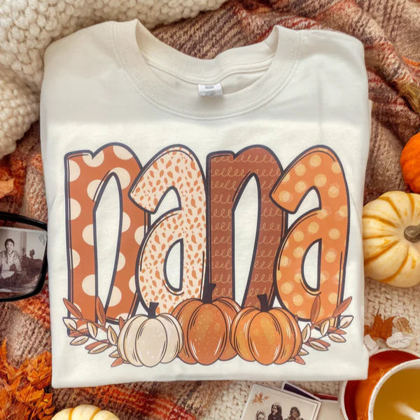 Folded sweatshirt with 'nana' and pumpkin design on a fall-themed background with pumpkins and leaves.