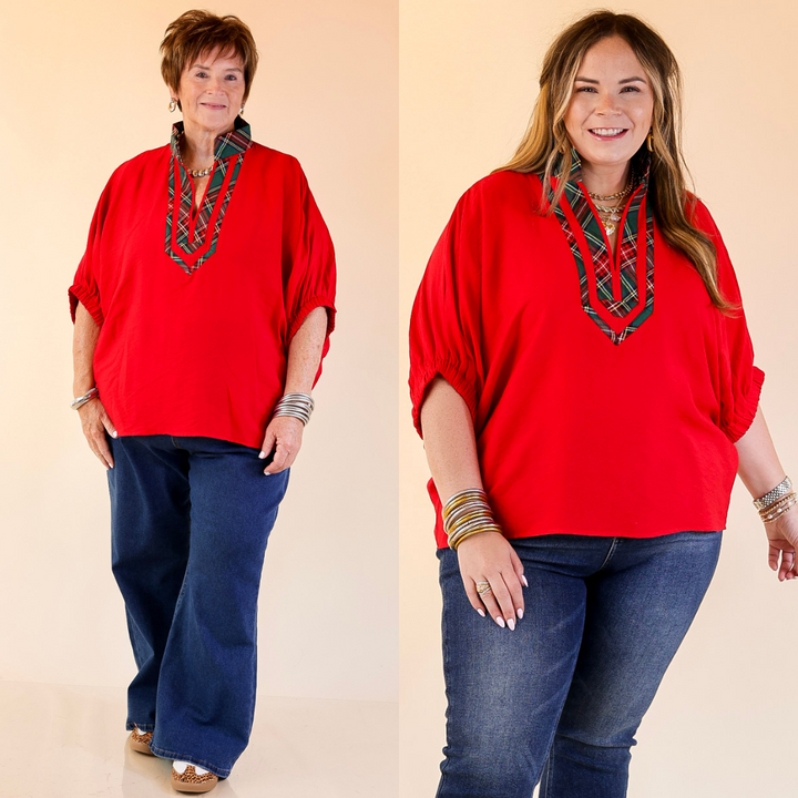 Two women wearing red poncho tops and blue jeans against a beige background