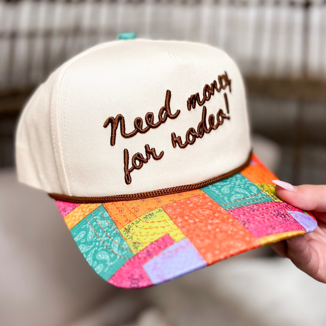 Colorful cap with text Need Money for Rodeo held by a hand against a neutral background