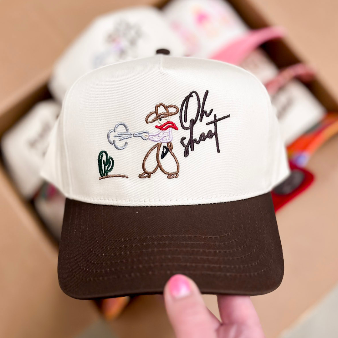 Cream embroidered Oh Shoot trucker hat with western graphic design and brown brim.