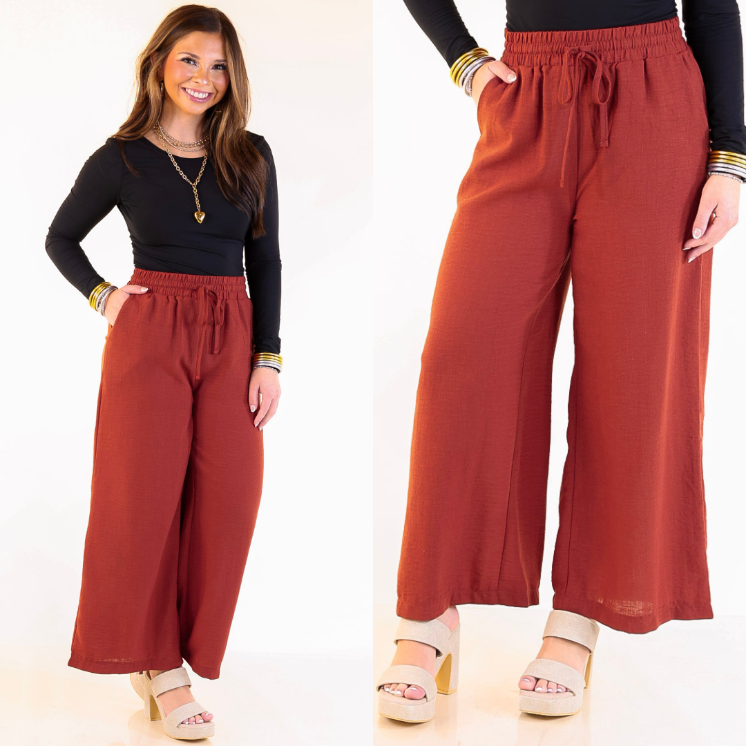Woman wearing rust cropped woven pants on a white background