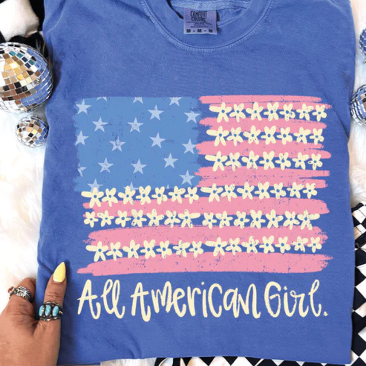 Comfort Colors graphic t-shirt featuring a floral American flag design with All American Girl text in multiple color options.