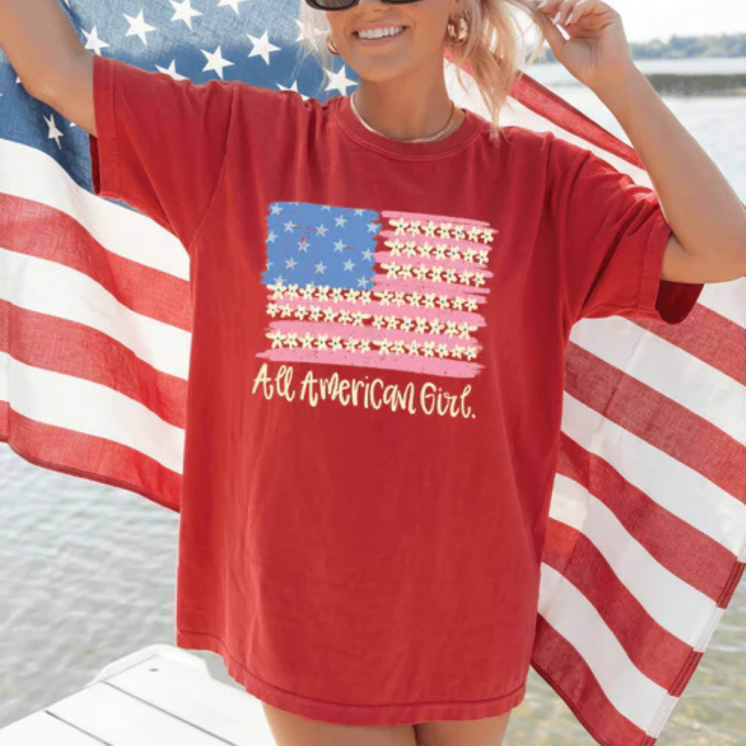 Comfort Colors graphic t-shirt featuring a floral American flag design with All American Girl text in multiple color options.