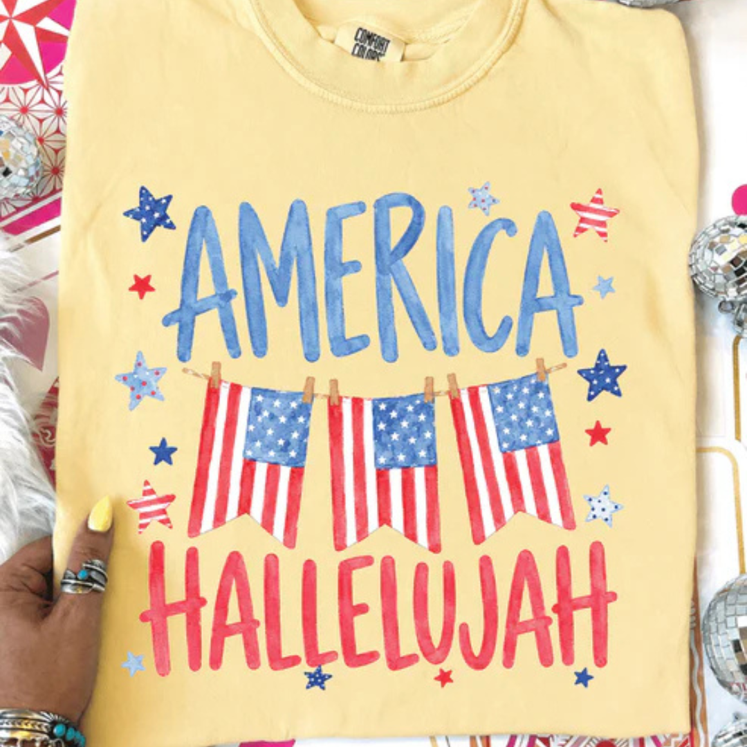 Butter yellow graphic tee featuring an America Hallelujah design with American flag bunting, patriotic stars, and red, white, and blue lettering.
