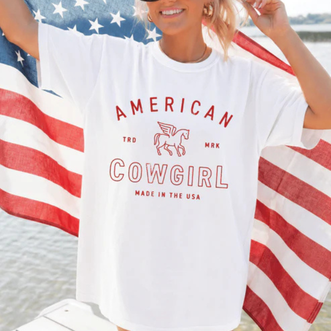 White Comfort Colors graphic t-shirt featuring American Cowgirl lettering with a vintage horse emblem and Made in the USA patriotic design.