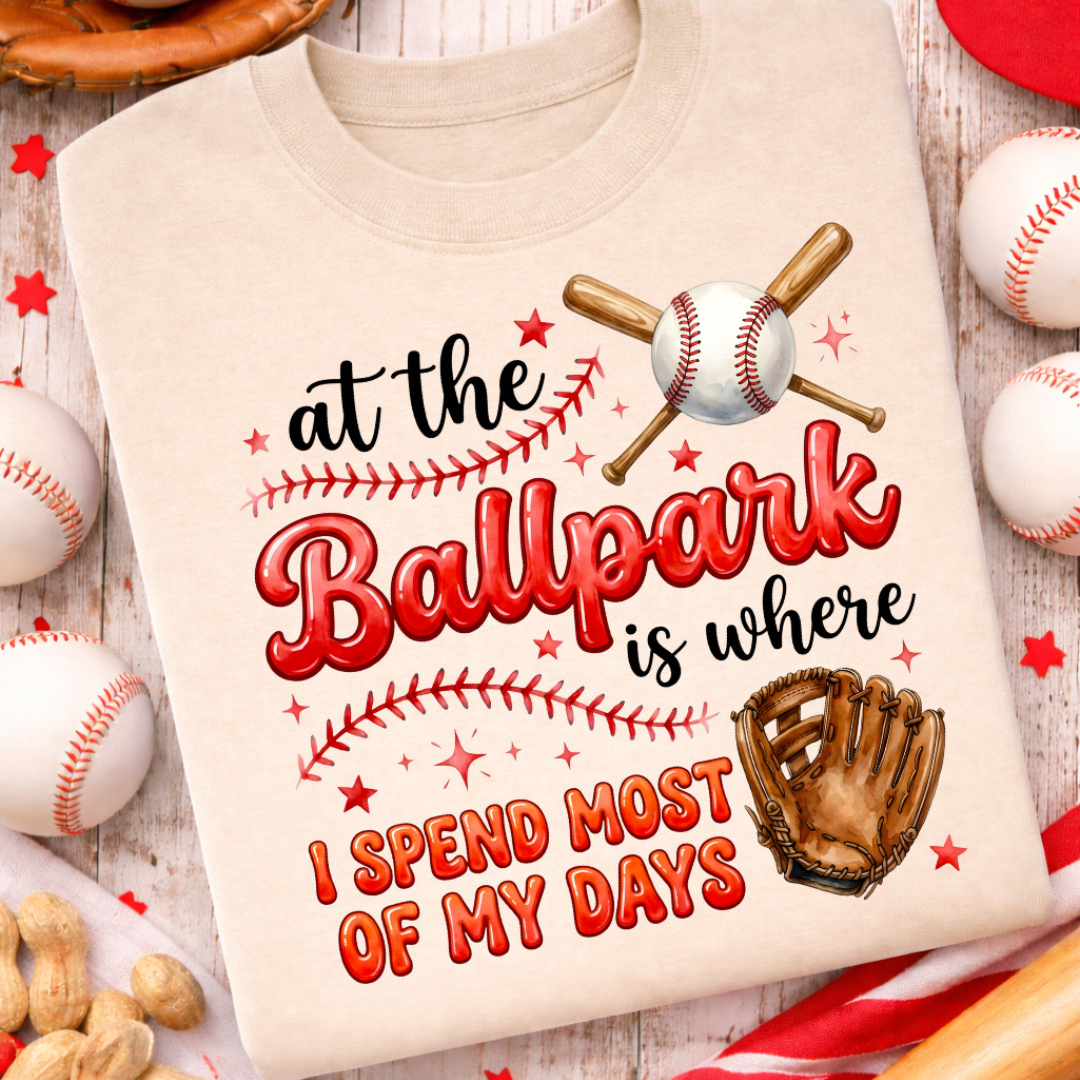 Sand graphic tee featuring the phrase "At the Ballpark is Where I Spend Most of My Days" with crossed baseball bats, baseball, glove, baseball stitching, and red star accents.