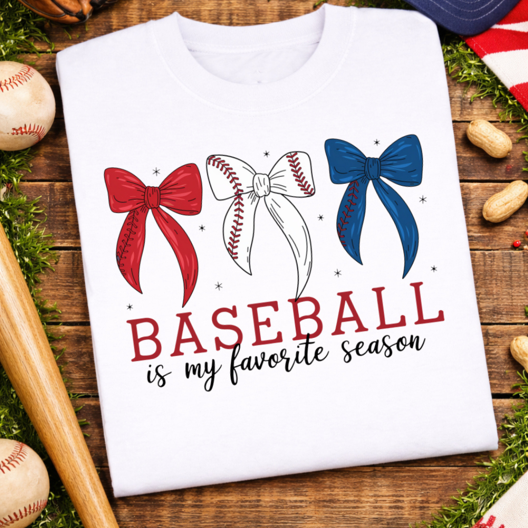 White graphic tee featuring the phrase "Baseball Is My Favorite Season" with three red, white, and blue bows, including a baseball stitch bow.