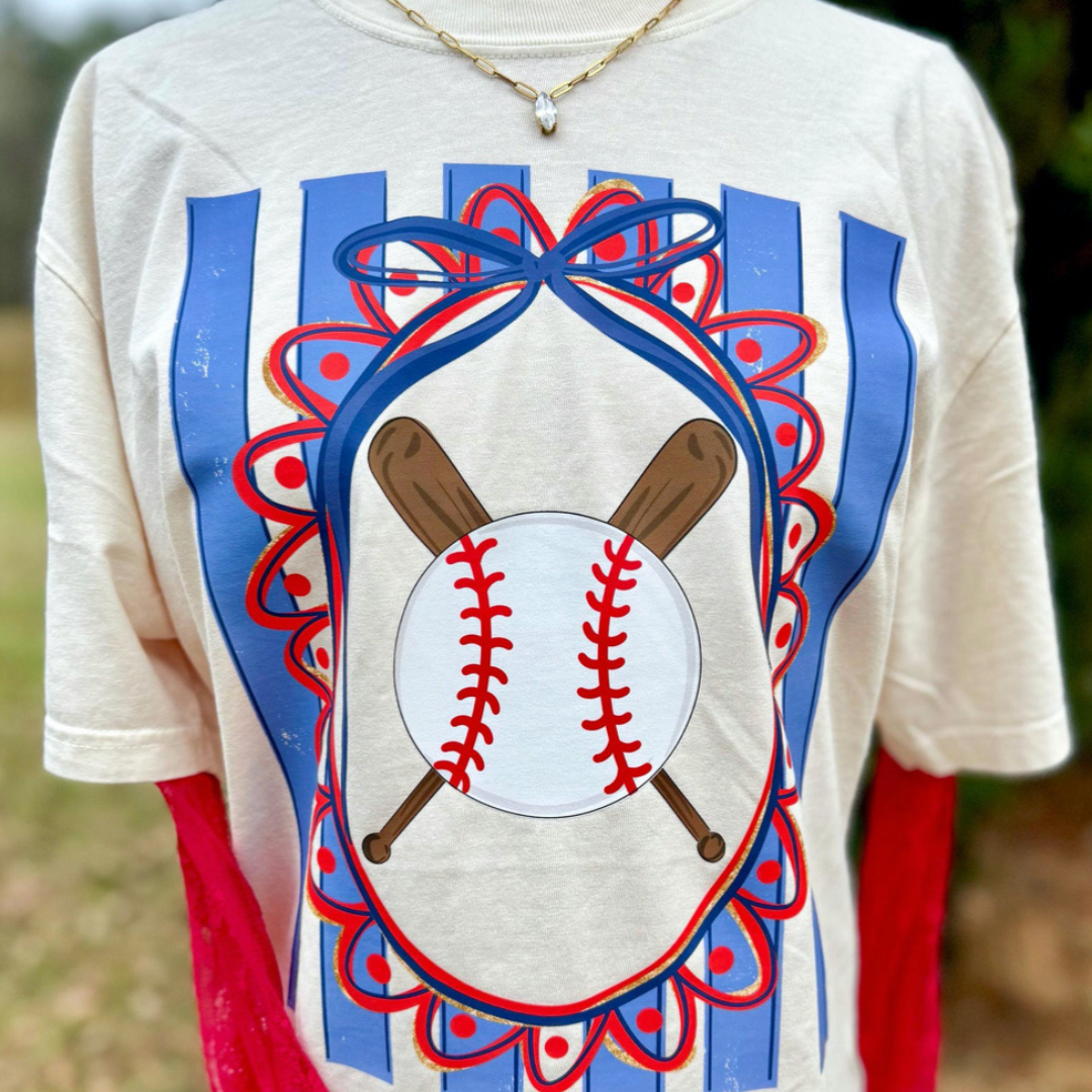 Natural graphic tee featuring a patriotic baseball design with crossed baseball bats, a red, white, and blue bow, scalloped frame, and blue stripe background.