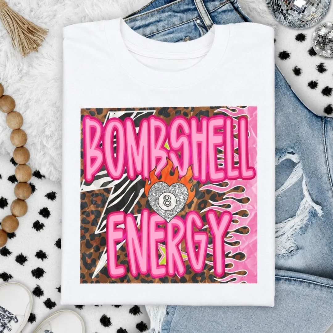 White graphic tee featuring a bold pink Bombshell Energy design with leopard print, zebra print, and flaming lucky number graphic.