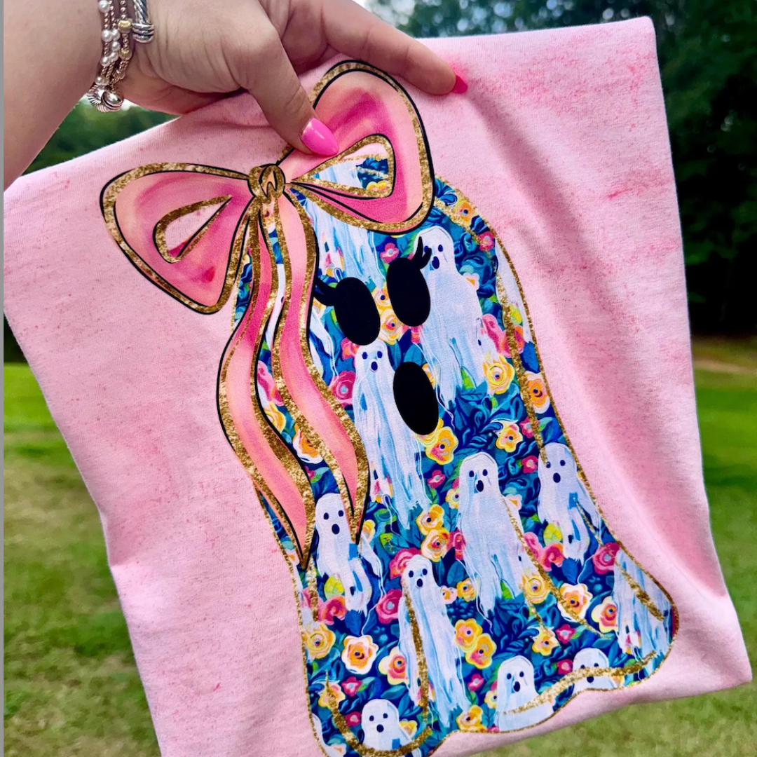 Light pink Halloween graphic tee featuring a floral ghost with an oversized pink bow, gold accents, and a whimsical ghost and floral pattern.
