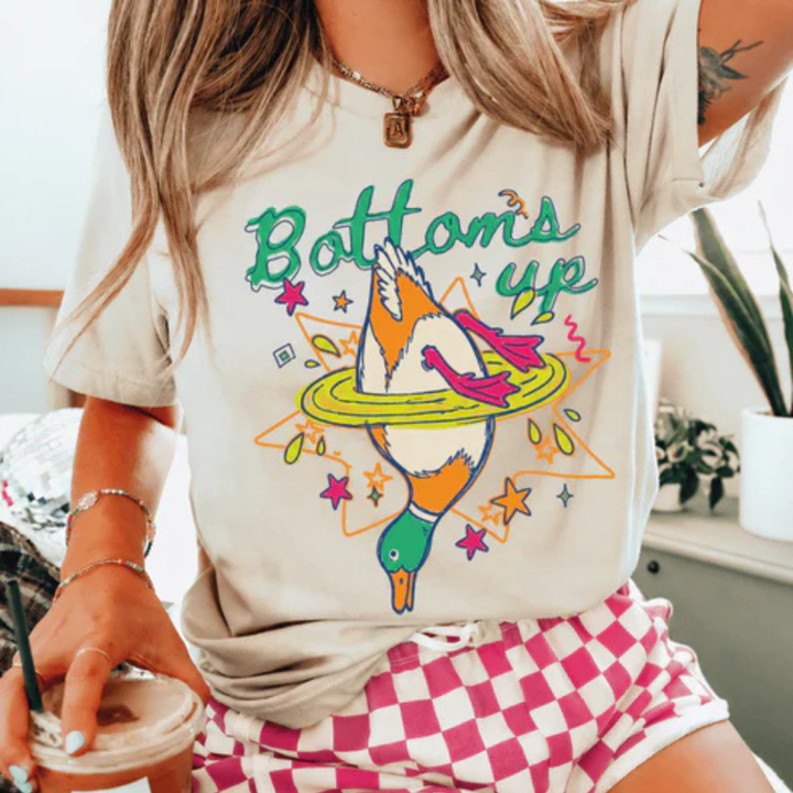 Graphic t-shirt featuring a colorful upside-down mallard duck splashing into water with Bottoms Up text in multiple color options.