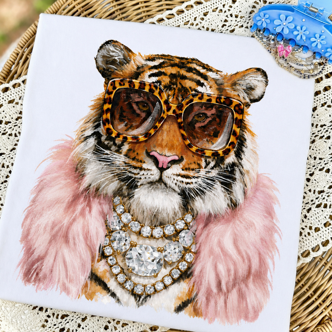 White graphic tee featuring a stylish tiger wearing leopard print sunglasses, layered jewels, and a pink faux fur stole.