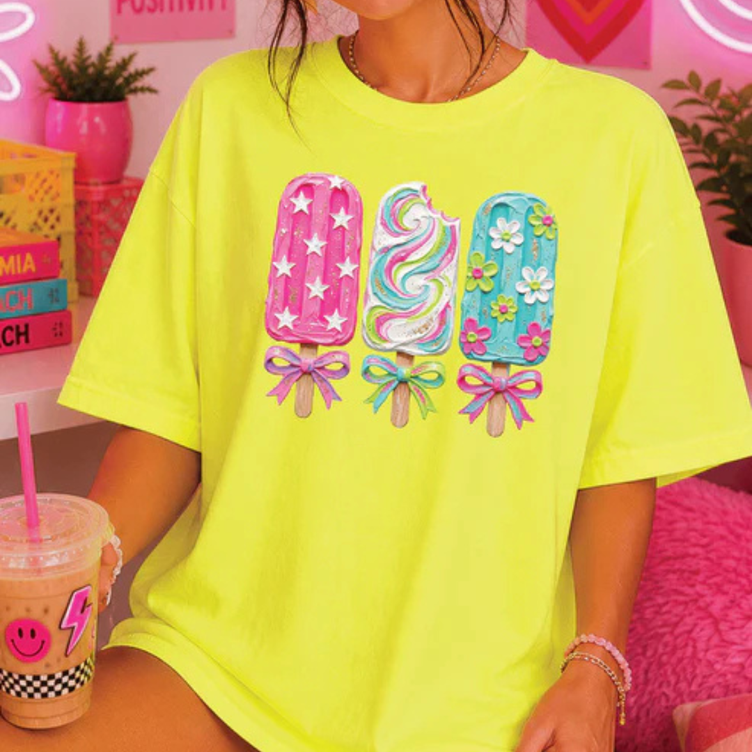 Neon yellow graphic tee featuring three colorful decorated popsicles with floral, star, and bow accents.