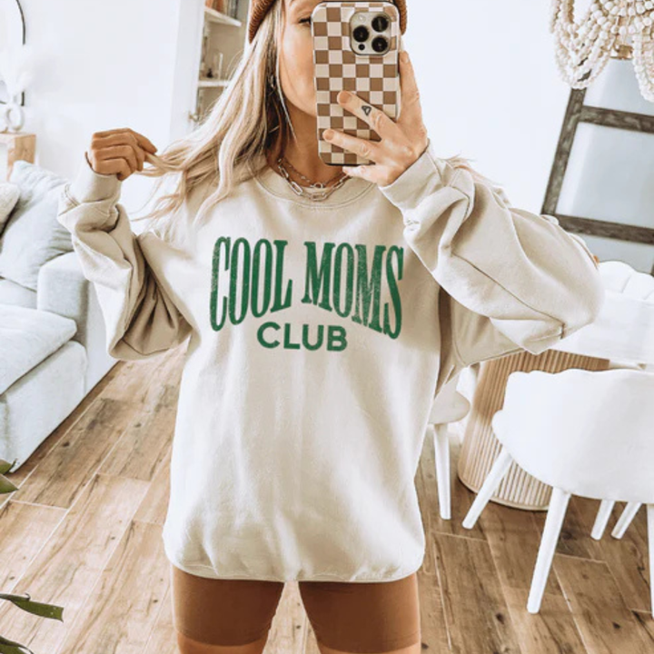 Cream graphic tee and sweatshirt featuring a bold vintage-style Cool Moms Club design in green lettering.
