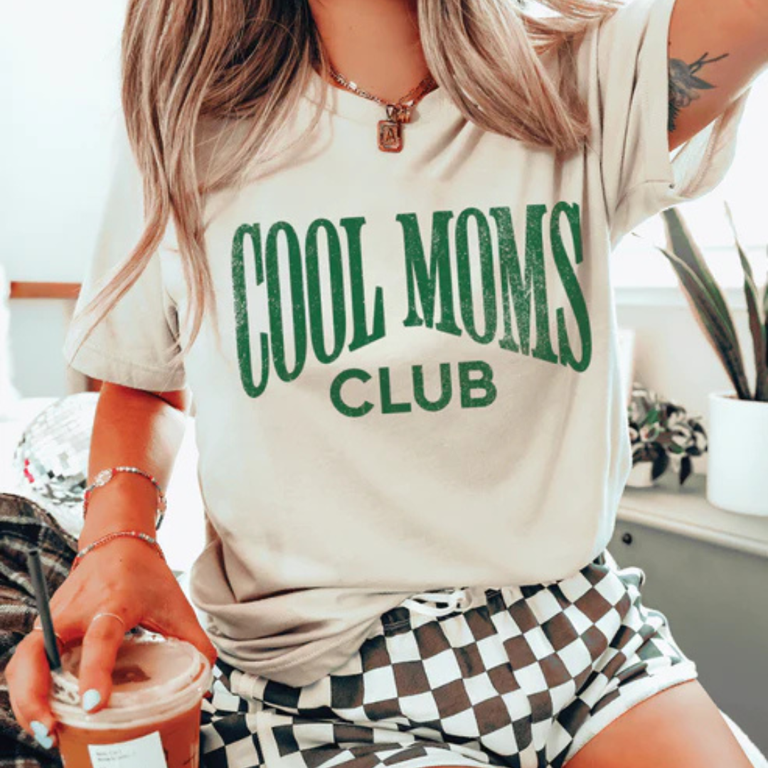 Cream graphic tee and sweatshirt featuring a bold vintage-style Cool Moms Club design in green lettering.
