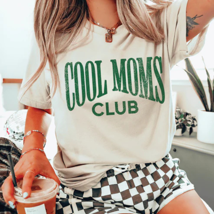 Cream graphic tee and sweatshirt featuring a bold vintage-style Cool Moms Club design in green lettering.