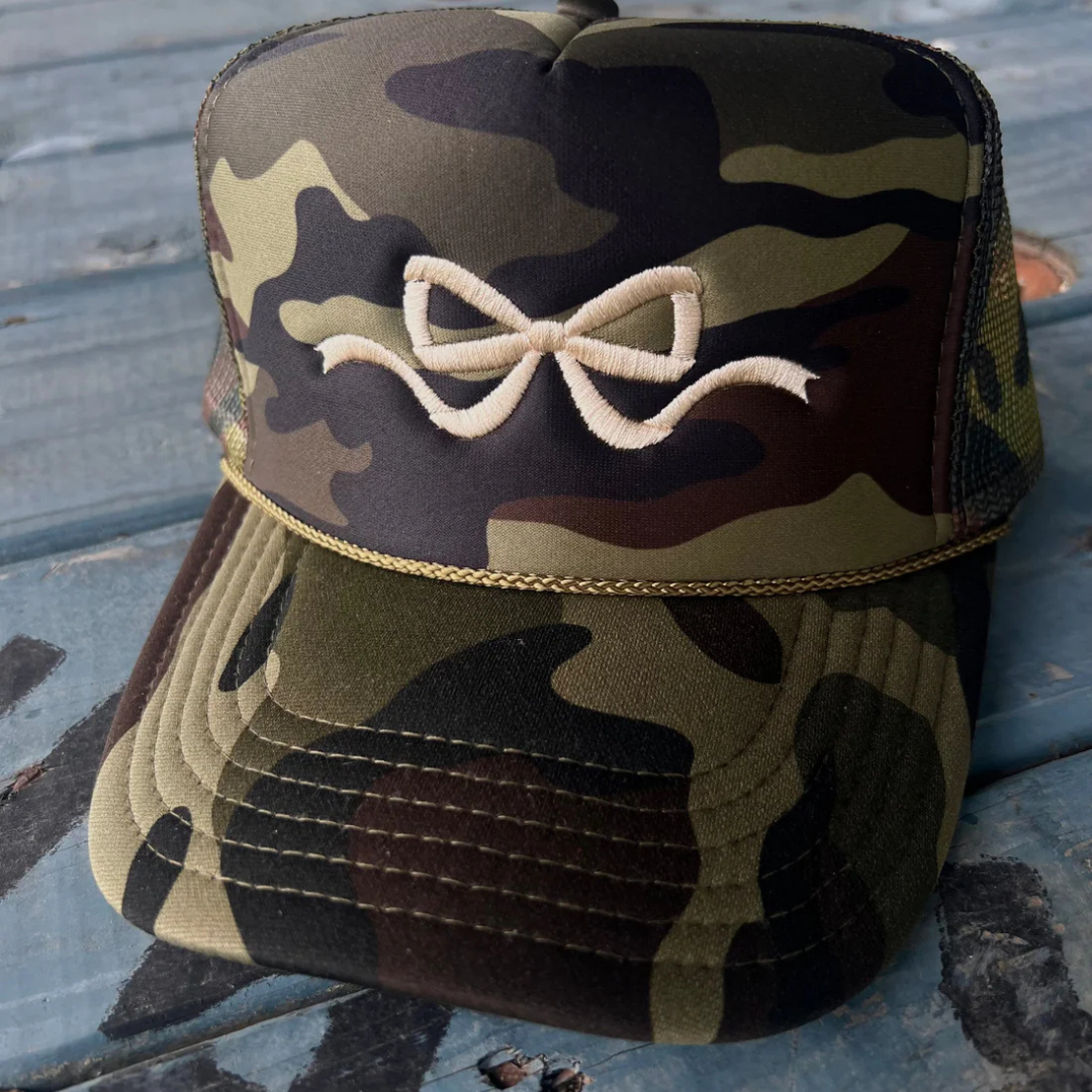 Camouflage trucker hat featuring a feminine embroidered bow design with an adjustable mesh back.