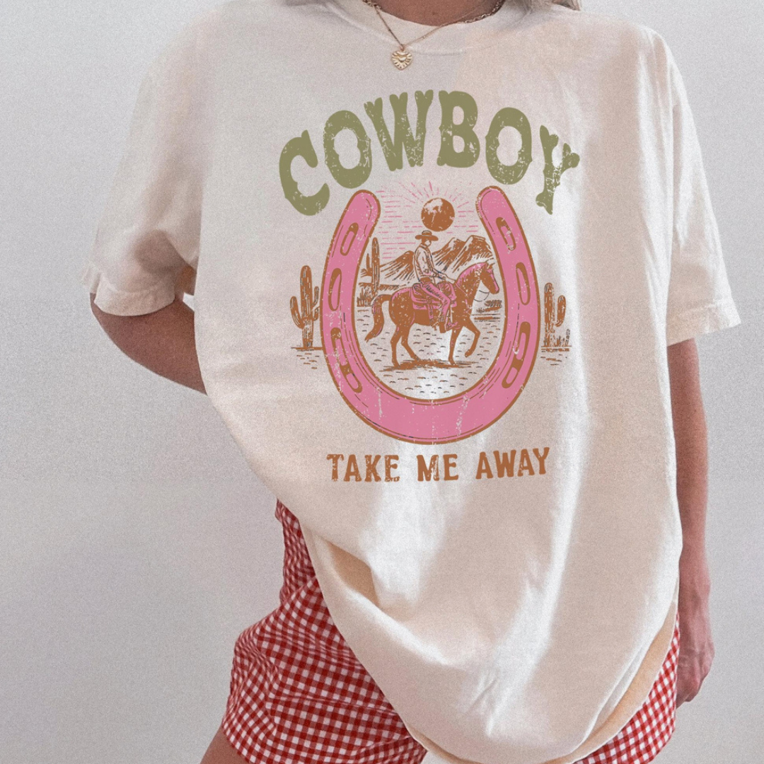 Natural graphic tee featuring a vintage cowboy scene inside a pink horseshoe with the phrase "Cowboy Take Me Away."