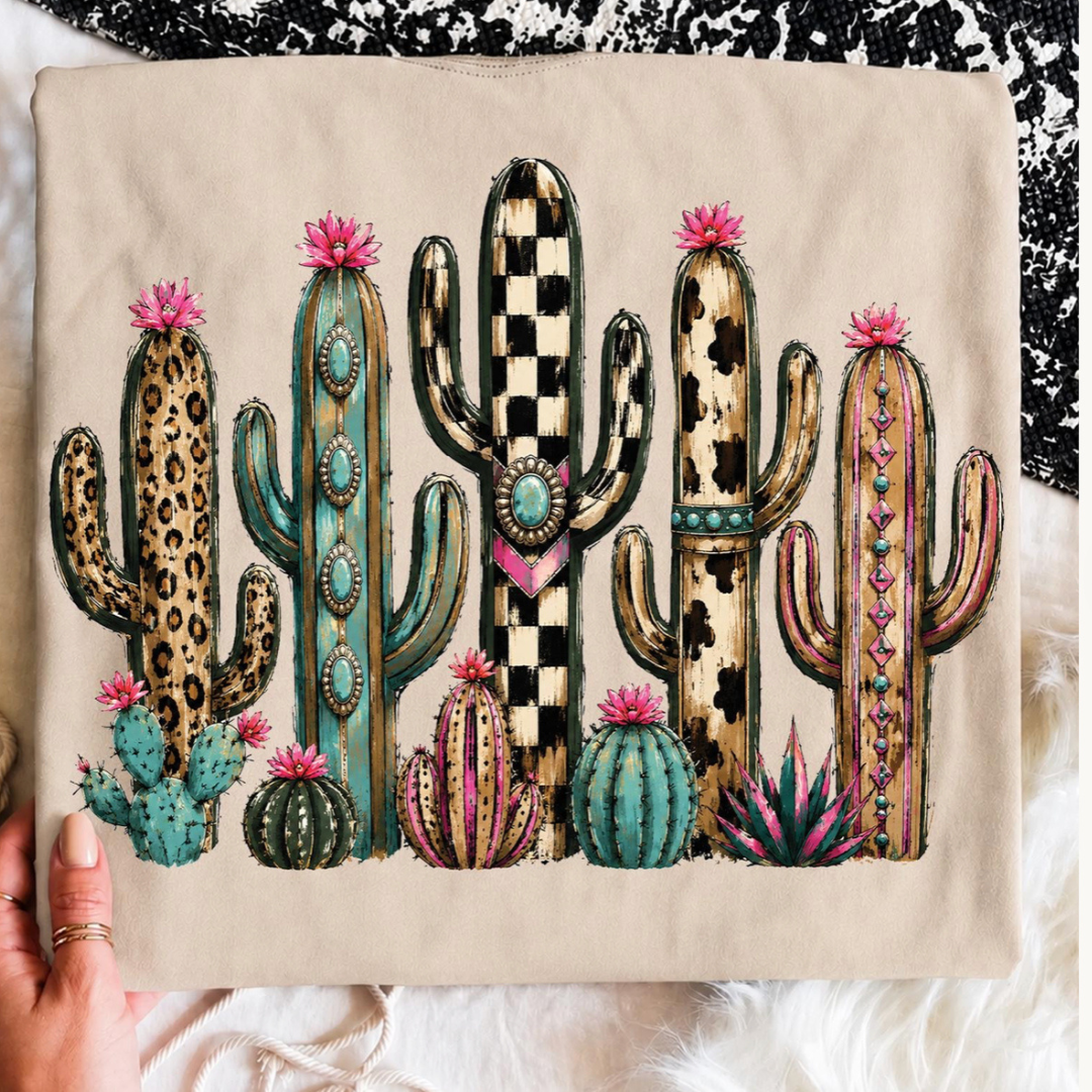 Natural graphic tee featuring a colorful collection of western-inspired cacti with leopard, checkerboard, cowhide, and turquoise accents.