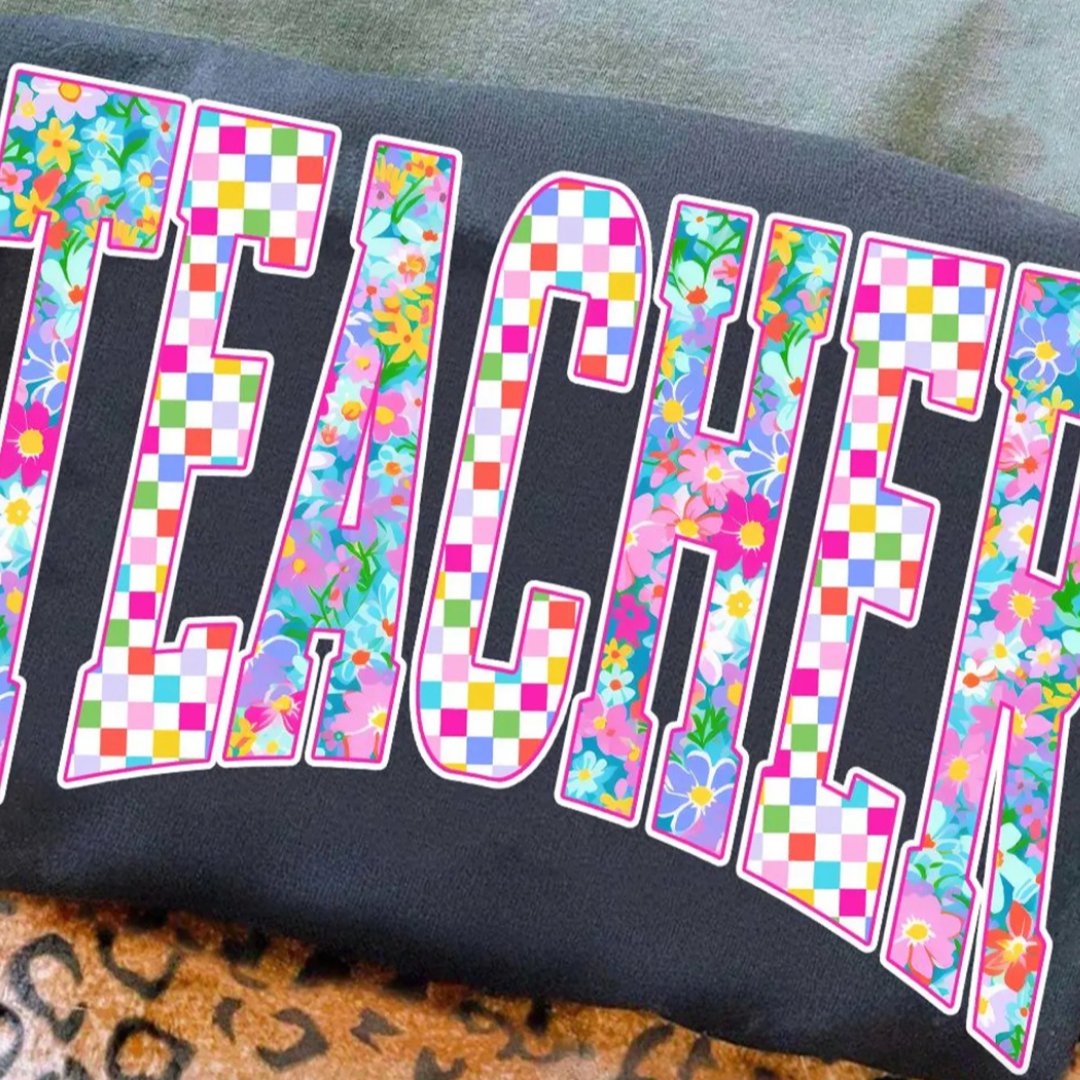 Black graphic tee featuring oversized varsity-style "Teacher" lettering filled with colorful floral and checkered patterns.